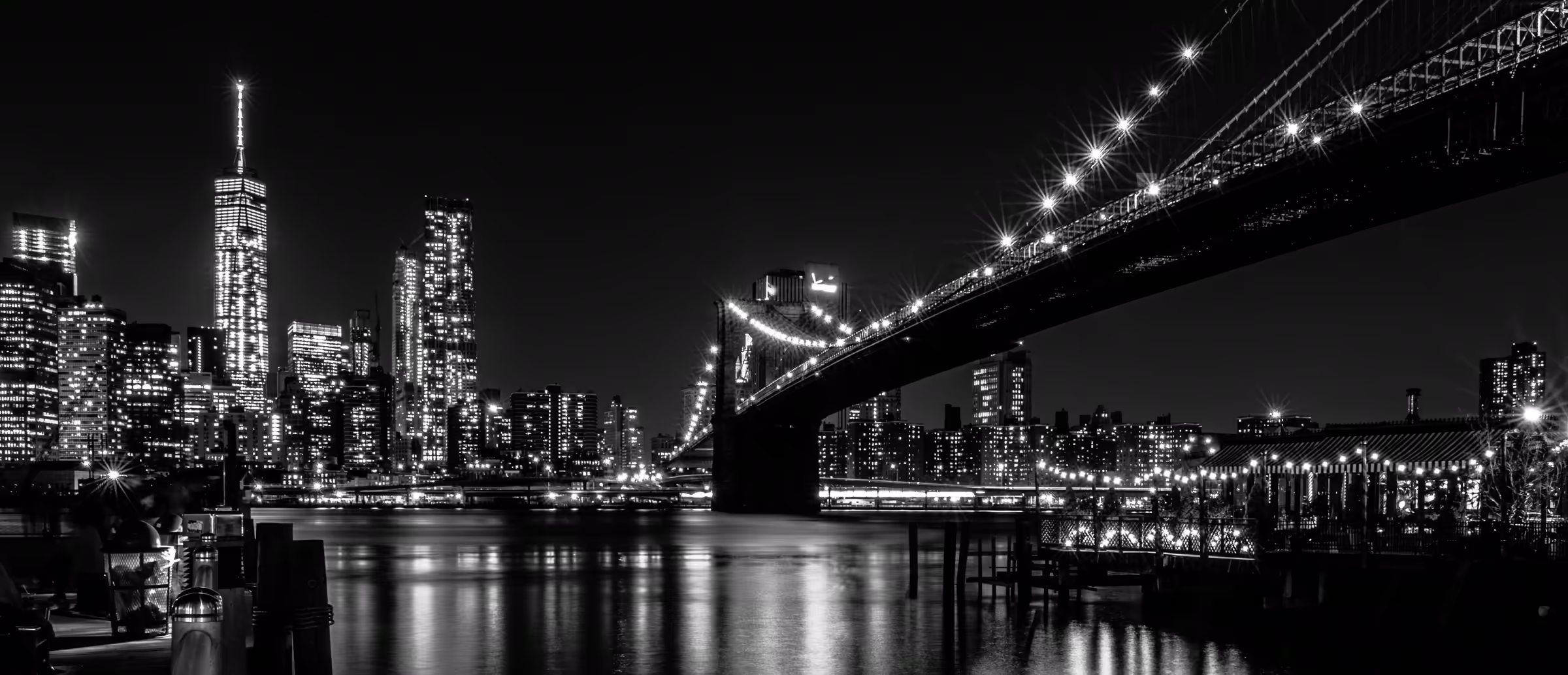 Monochrome cityscape featuring the Brooklyn Bridge's Gothic Revival architecture illuminated against the Manhattan skyline.